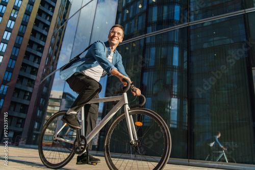 Bild auf Leinwand A man rides his bicycle through an urban business district, smiling confidently in the sunlight