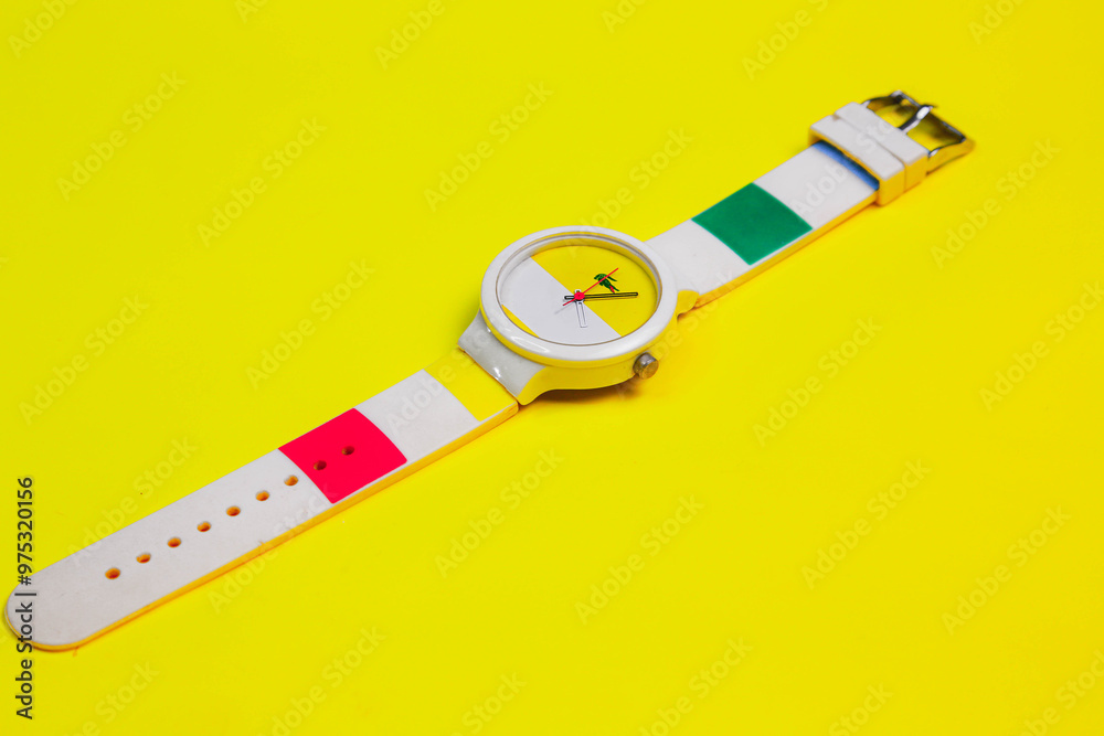 A stylish wristwatch with a colorful striped band and minimalist dial, set against a bright yellow background. A stylish wristwatch with a colorful striped band and minimalist dial, set against a bright yellow background.