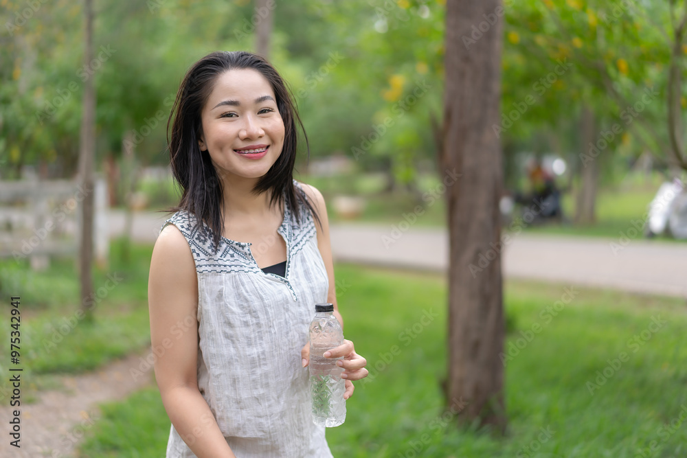Happy young woman holding a water bottle in her hand Her cheerful demeanor and relaxed demeanor reflect the happiness she finds in her peaceful surroundings. during the summer Lifestyle of happiness. Happy young woman holding a water bottle in her hand Her cheerful demeanor and relaxed demeanor reflect the happiness she finds in her peaceful surroundings. during the summer Lifestyle of happiness.