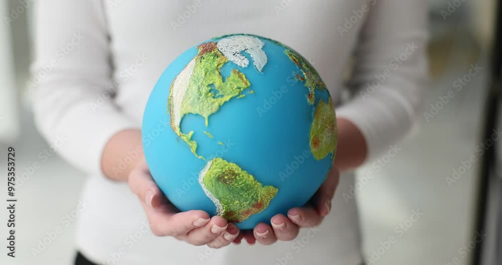 Woman holds model of Earth and examines details of oceans. Female dressed in white jumper looks at continents and oceans painted with precision Woman holds model of Earth and examines details of oceans. Female dressed in white jumper looks at continents and oceans painted with precision