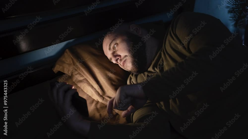 Tired man lying in bed sleepless holding smartphone in hand scrolling social media, suffer sleep disorder in dark bedroom. Man need rest. anxiety, sleeplessness and depression concept