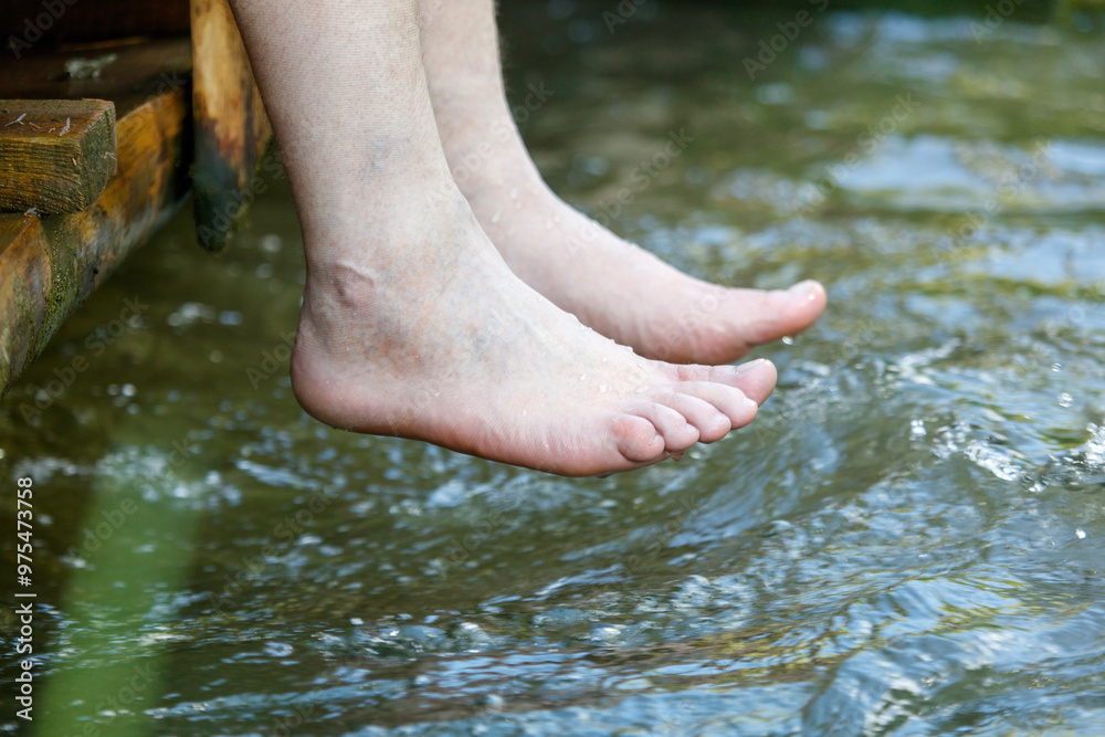 A man's bare feet hang into the river water A man's bare feet hang into the river water