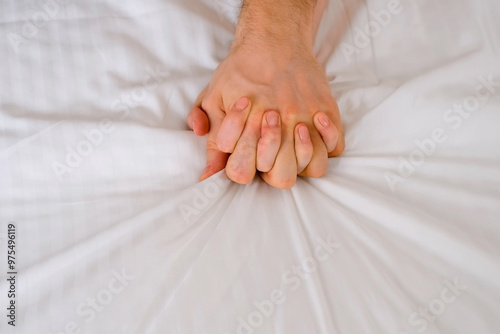 Φωτογραφία Man and woman holding hands lying in bed making love, hands close-up