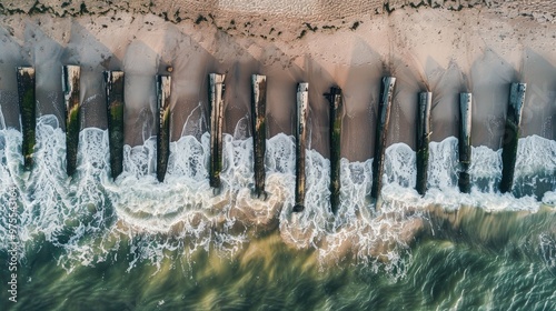 Fototapeta Naklejka Na Ścianę i Meble -  Top view of weathered wooden breakwater piles on the Baltic Sea shoreline with gentle waves on sandy beach during the day