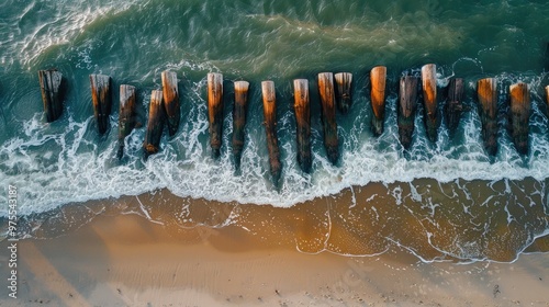 Fototapeta Naklejka Na Ścianę i Meble -  Top view of weathered wooden breakwater piles on the Baltic Sea shoreline with gentle waves on sandy beach during the day