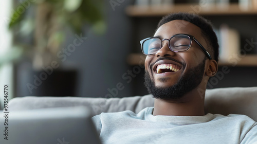 A man laughs heartily while enjoying a humorous clip on his laptop in a cozy living room setting during a leisurely afternoon