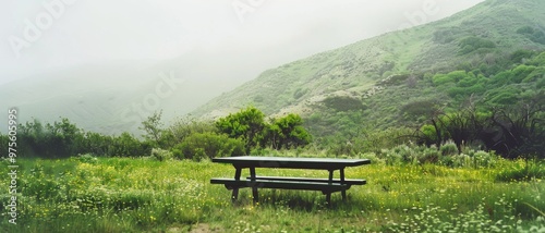 A solitary picnic table stands in a lush, green meadow surrounded by misty hills, evoking a sense of peace and solitude in nature.