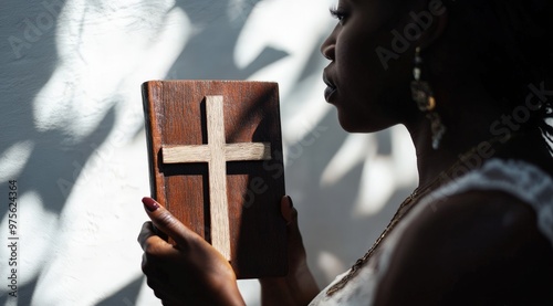 Woman holding wooden cross book with sunlit shadows on wall