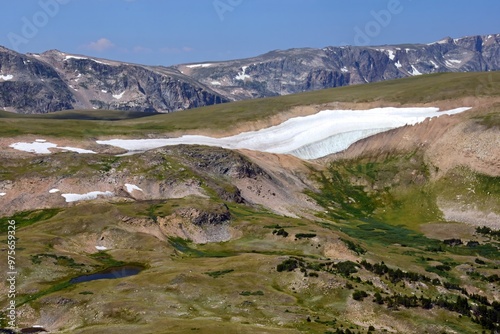 looking out across  alpine tundra, a lake, and a snow field to the mountains of the absaroka-beartooth wilderness on a sunny summer day, driving along the beartooth highway in wyoming