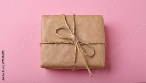 Small package or parcel in brown craft paper tied with jute rope. Eco-friendly. Pink backdrop.