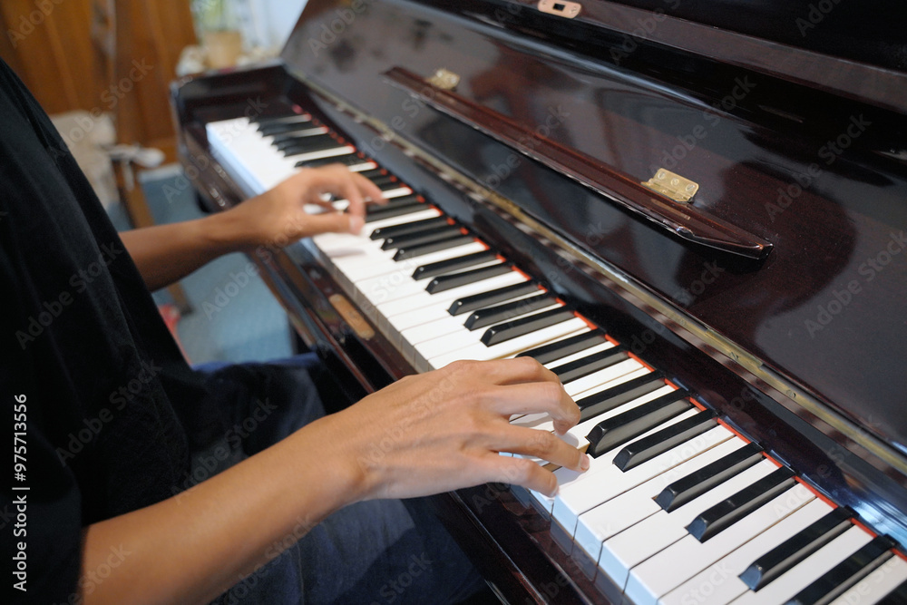 Obraz premium Close-up of a young Asian man touching the piano keys with his fingers, playing a musical composition while playing a grand piano in a cafe.