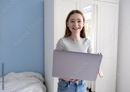 Teenage girl standing in bedroom with laptop photo