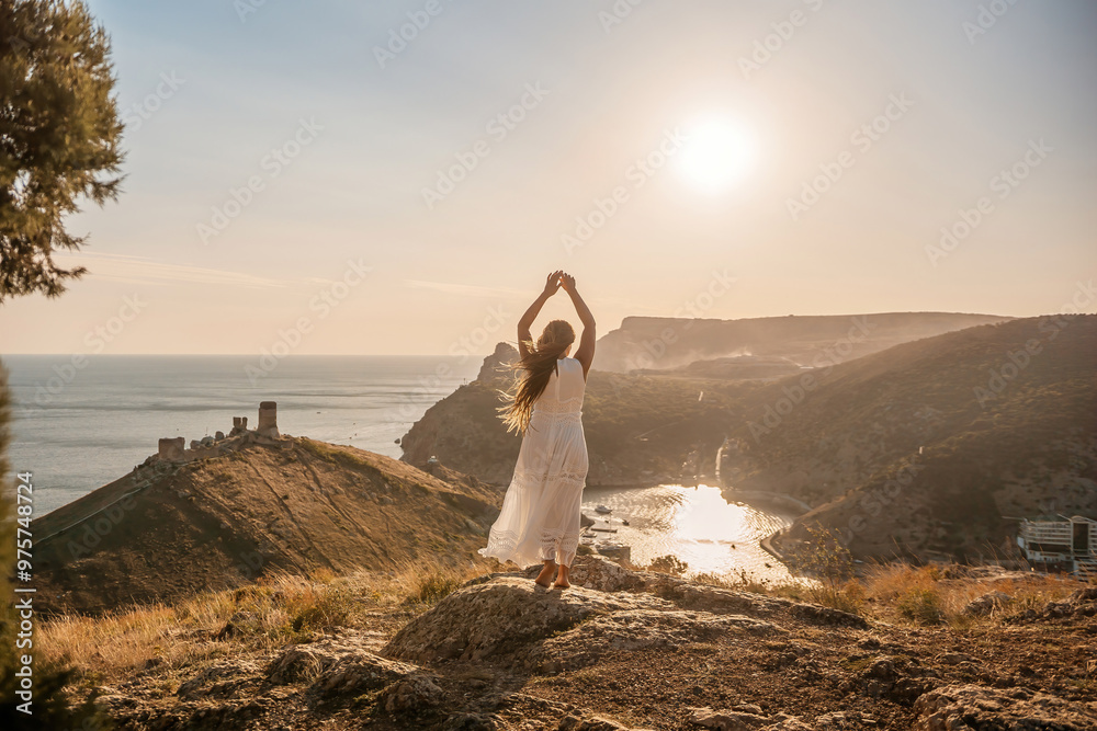 woman stands on a rocky hill overlooking a body of water. She is wearing a white dress and she is in a state of joy or celebration. Concept of freedom and happiness. woman stands on a rocky hill overlooking a body of water. She is wearing a white dress and she is in a state of joy or celebration. Concept of freedom and happiness.