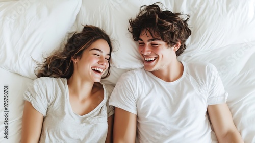 A young couple laughing and playfully teasing each other on a cozy white bed, radiating morning happiness.