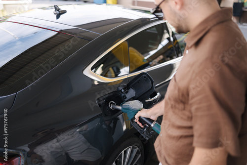 Handsome bearded man in sunglasses refueling his luxury car on self service gas station. Fuel price increase