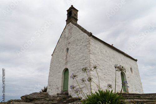 La petite chapelle Sainte-Barbe, aux murs extérieurs d'un blanc immaculé, se dresse majestueusement sur son rocher, face à la mer, en Bretagne.