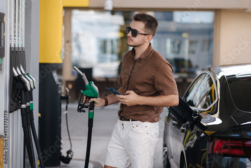 Handsome man in sunglasses hold green fuel pump in hand. Starting refueling car. Benzine photo