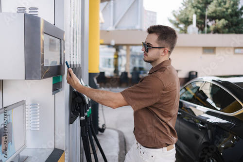 Man pay for petrol on self service gas station using his smartphone. Contactless payment. Fuel price increase