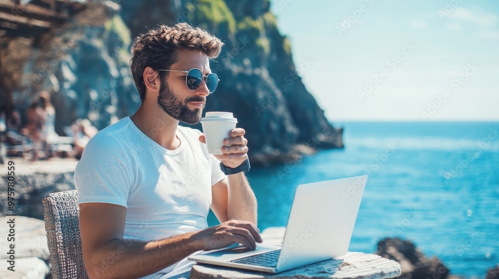 Fototapeta premium Thoughtful freelancer working on laptop at beach with coffee by the serene blue sea