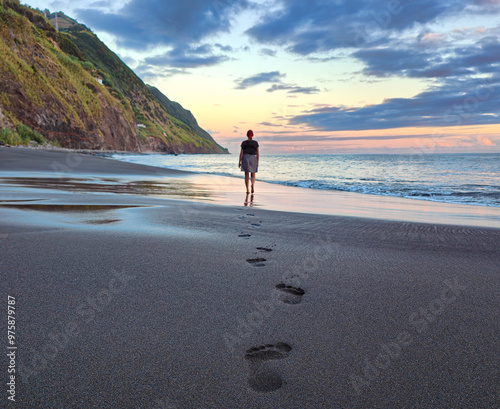 Silhouette of a young woman walking alone and leaving footprints on the sandy volcanic beach. Walking alone, getting away or wanderlust concept. Povoacao, Azores, Portugal