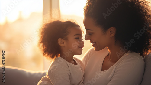 mother holding her daughter on a sofa, with both facing each other and sharing warm smiles. The setting should be a relaxed and homely living room, with gentle lighting to highligh photo