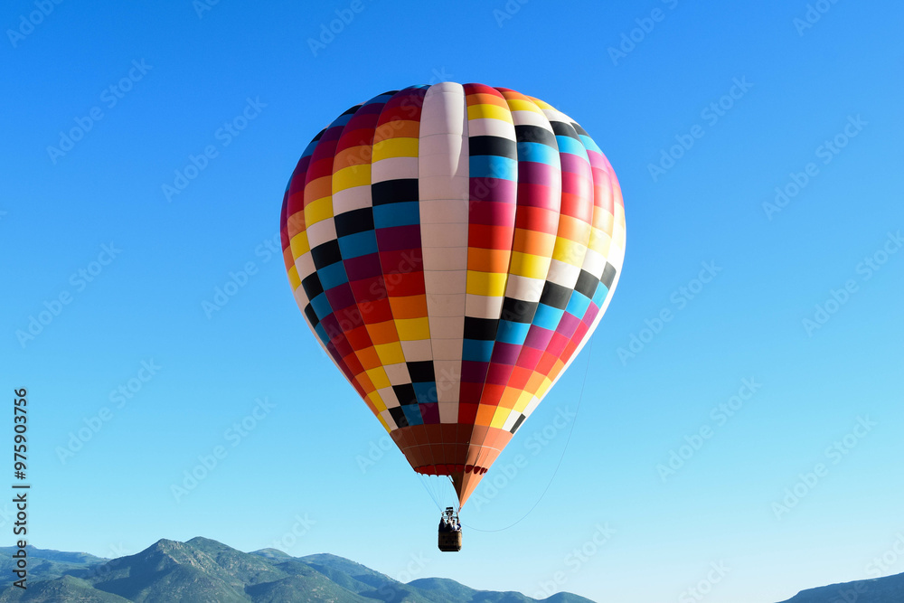 A colorful hot air balloon flying over the peaks of Utah on a bright blue sunny day A colorful hot air balloon flying over the peaks of Utah on a bright blue sunny day