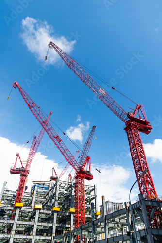 Low-angle view of cranes and steel structures of building construction with a blue sky background.