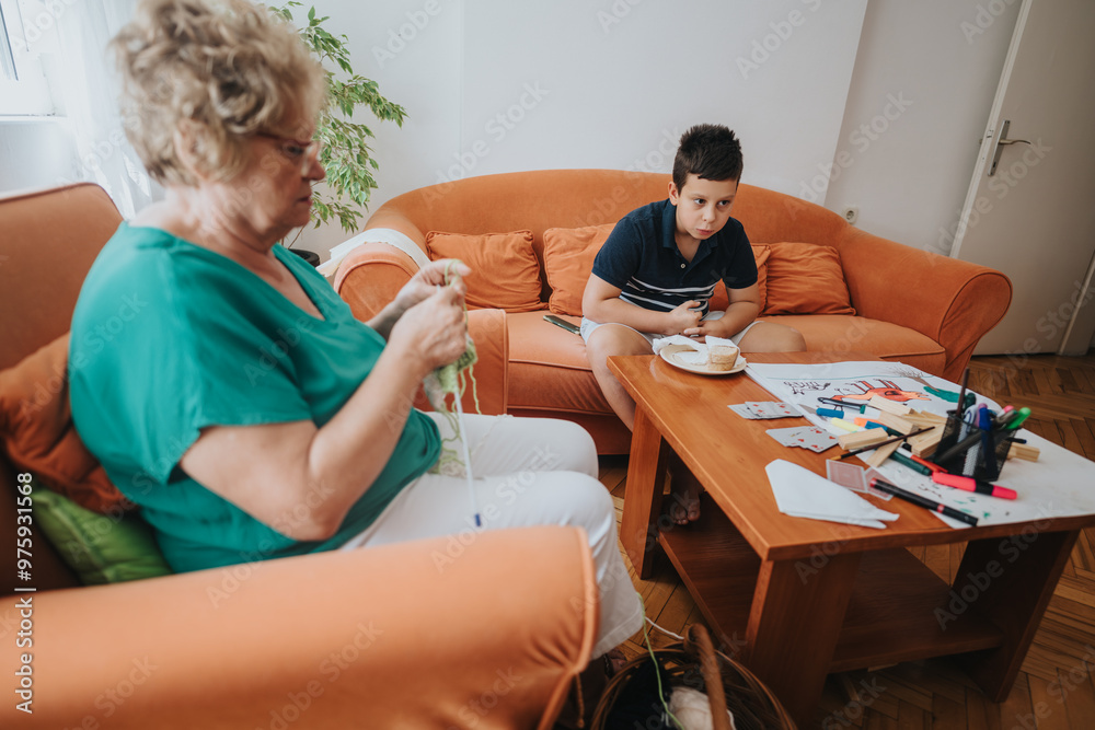 Obraz premium A grandmother sits on a sofa knitting a vest while her young grandson enjoys his meal at the table. The cozy scene captures family bonding moments.