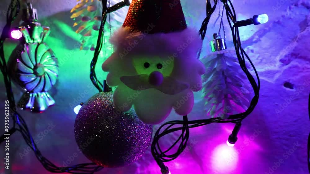 Una toma de cerca de una decoracion de navidad y fin de año con una cara de santa claus  rodeado de varias luces con bombillos de varios colores en movimiento en la oscuridad