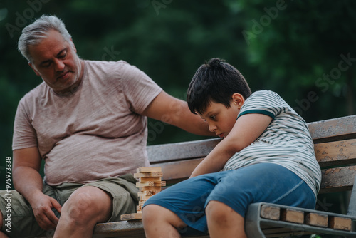 A father and son engage in a thoughtful game of building blocks on a park bench, enjoying quality time together on a peaceful day.