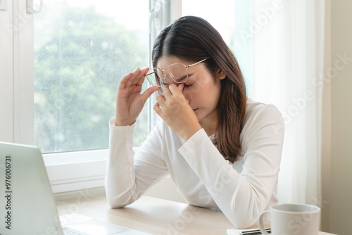 Eye problem concept, fatigue asian young woman tired eyes, irritated rubbing eye dry relief vision pain after work on laptop computer, eye strain, hand holding glasses, suffer migraine, bad blurry