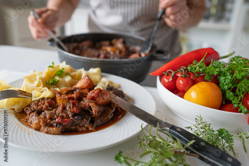 Homemade food with delicious braised beef slice legs, sauce and pasta served by a woman with apron in the kitchen for dinner