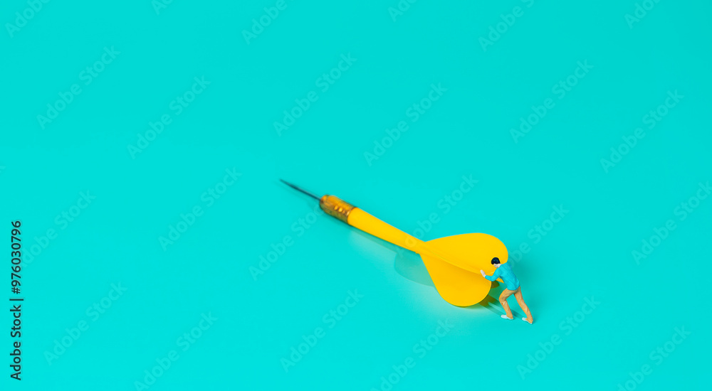 a miniature figure of a person pushing. overcoming challenges or striving toward a goal. with the dart symbolizing precision and targets, while the small figure suggests perseverance or effort.