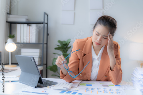 Businesswoman in an orange jacket checking the document on her desk, holding glasses, feeling Eye strain in the office. photo