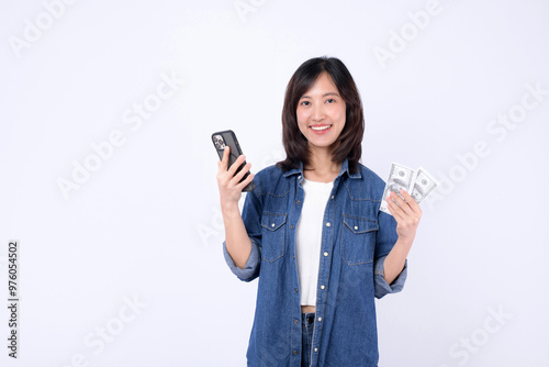 A young woman is smiling while holding smartphone in one hand and cash in other, showcasing sense of financial success and happiness