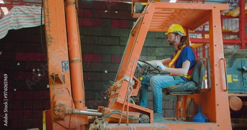 A construction worker in a hard hat and safety vest operating a forklift Heavy Machinery in an industrial warehouse.