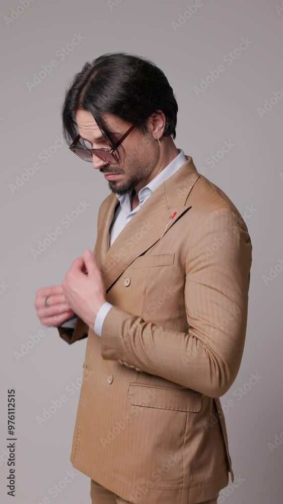 side view of attractive model fixing his double breasted brown suit collar and holding pockets on gray background side view of attractive model fixing his double breasted brown suit collar and holding pockets on gray background
