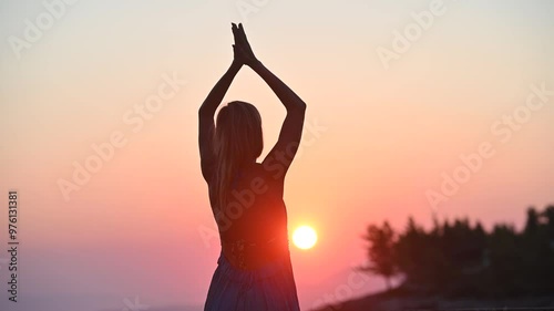 Footage of a young woman in summer dress meditating at warm sunrise