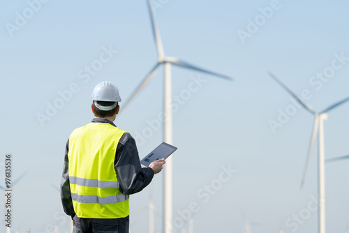 Engineer with digital tablet works on a field of wind turbines