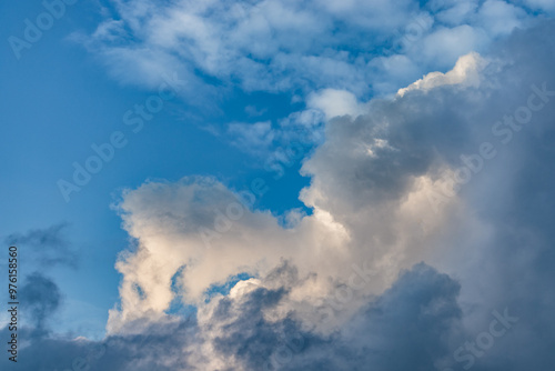 A stunning image of a vibrant blue sky with dramatic cumulus clouds. Sunlight softly illuminates the clouds, creating a tranquil, atmospheric scene, ideal for nature, weather, or serene backgrounds.