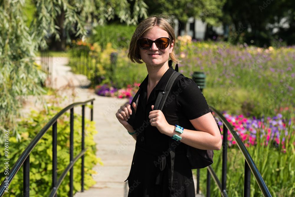 Fototapeta premium Attractive thirty year old woman with sunglasses and a black dress posing in the botanical garden during summer