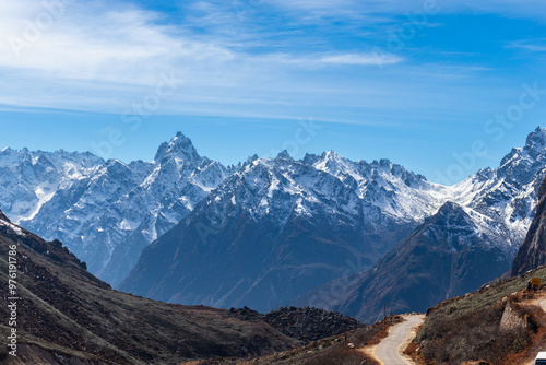 A stunning view of snow-capped mountains under a clear blue sky. Rugged peaks and a winding path create a picturesque scene, ideal for travel, adventure, nature, and outdoor themes, Sikkim, India