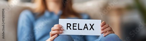 Person holding a white card with the word relax, promoting stress relief and relaxation in a cozy, comfortable setting.