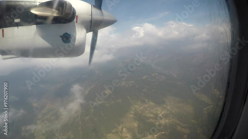 High angle view through dirty porthole of flying passenger aircraft of green mountain valley and clouds during flight between Ramecchap and Lukla. Handheld video. Travel in Nepal for trekking theme. photo