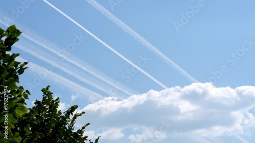 Airplane condensation trails (contrails) in the blue sky going out of a cloud