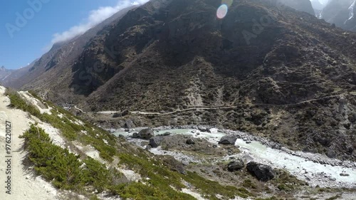 Panoramic spinning view of dirt footpath in mountain view next to Thyangmoche village and flowing Bhote Koshi river in Himalayas in Nepal in a sunny day. Snowcapped Kongde Ri mountain in background.