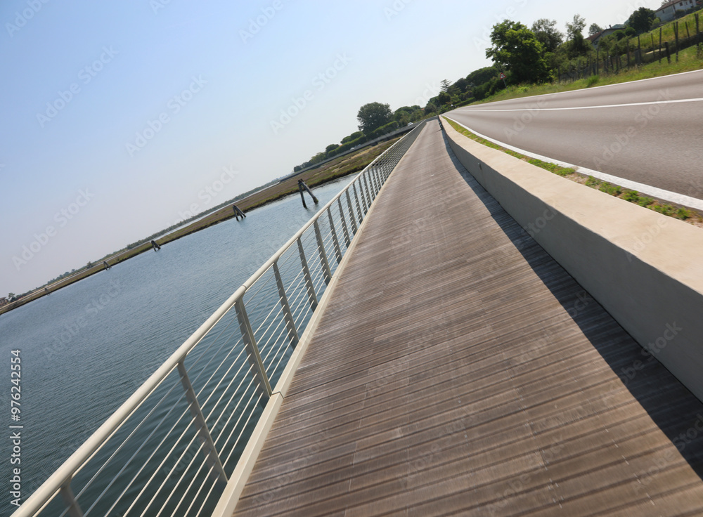 Fototapeta premium intentionally tilted photo of the new cycle path made of wood and steel railings that runs along the Venetian lagoon at Treporti near Jesolo and the island of Venice