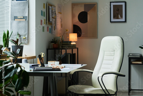 Contemporary home office featuring white ergonomic chair, desk with various office supplies, bookshelves and soft lighting