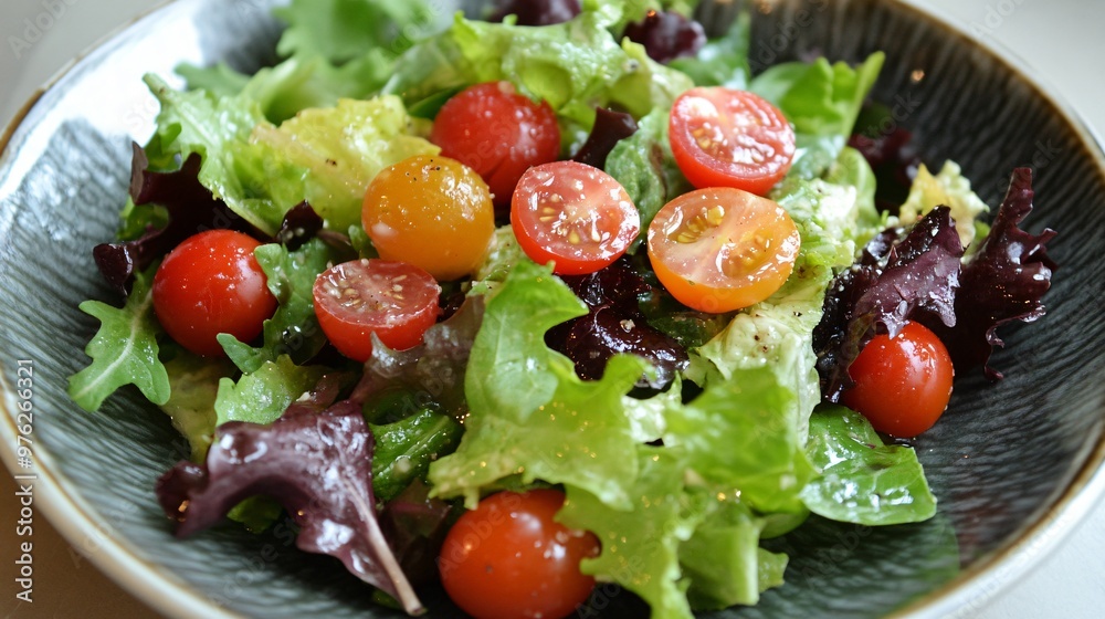 Close-up of a fresh salad with cherry tomatoes and mixed greens in a gray bowl.