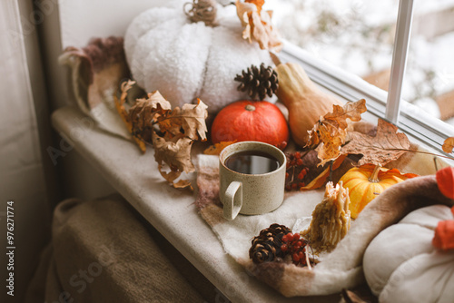 Autumn still life. Warm cup of tea, pumpkins, fall leaves, candle and woolen scarf on windowsill. Autumn hygge. Happy Thanksgiving